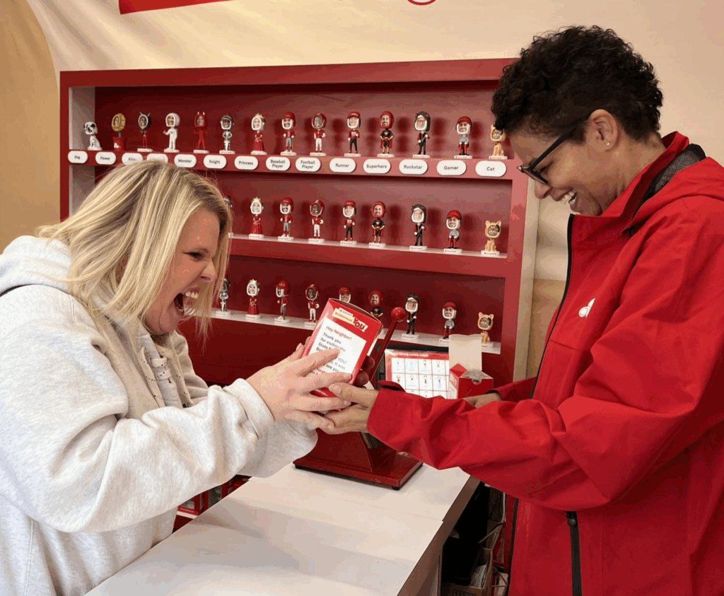 A fan reacts with delight as a State Farm team member hands over her bobblehead order.