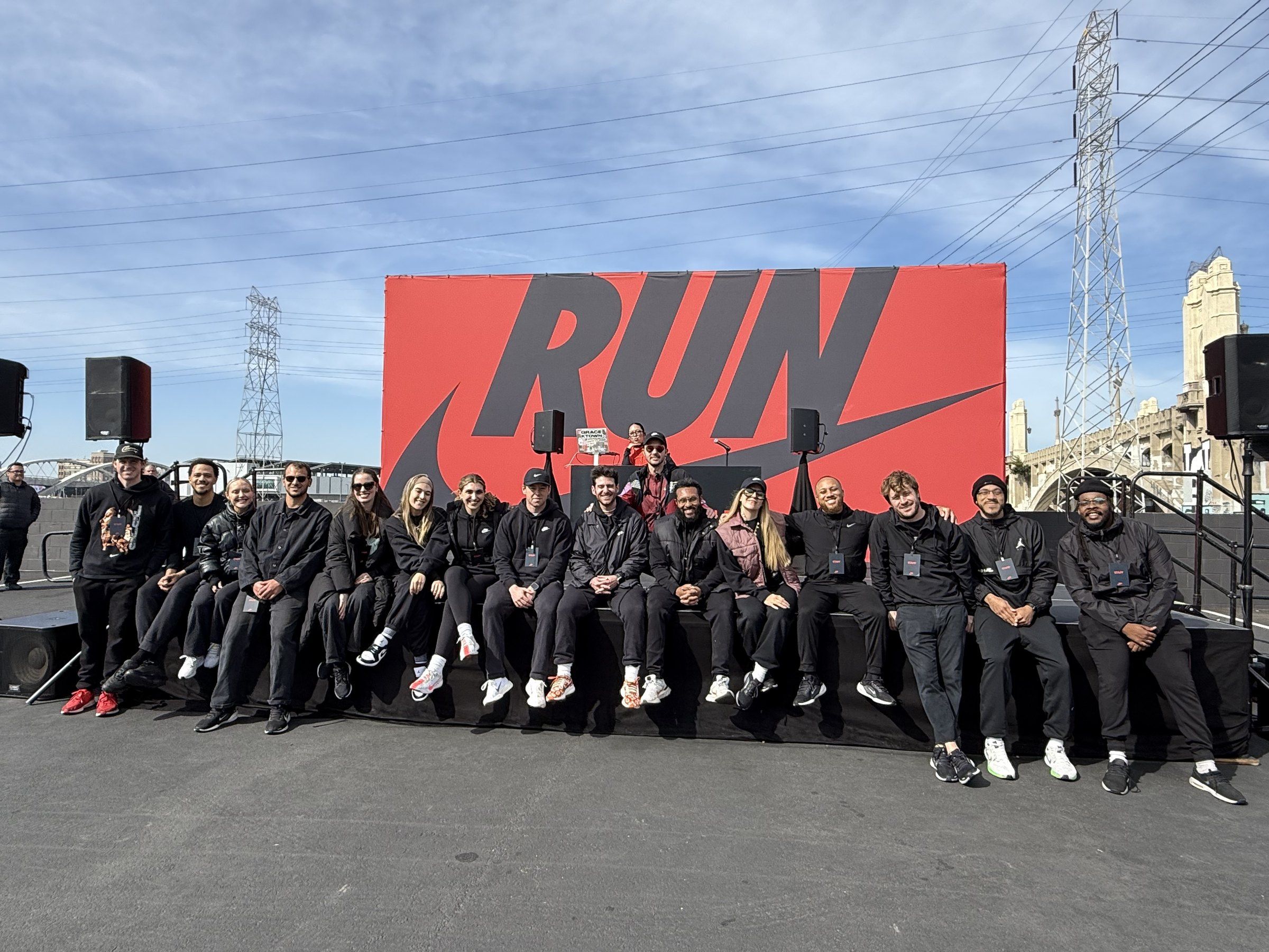 A crew in black sits in a row along the edge of an event stage.