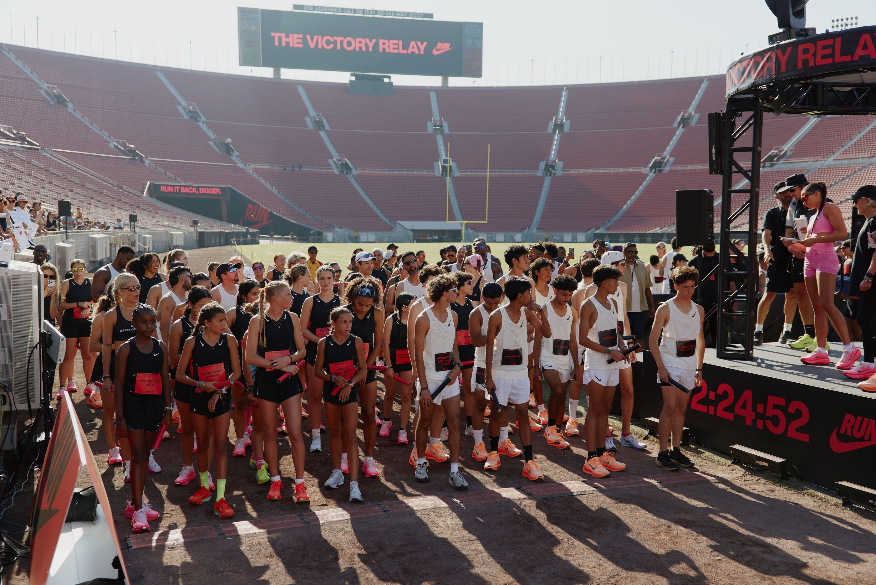 Relay runners gathered at the start line inside the LA Memorial Coliseum, beside a race clock reading 2:24:52.